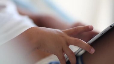 Child hands holding tablet playing game. Kid close-up hands using tech device