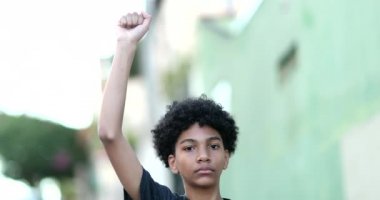 Young black boy raising fist in the air, kid looking at camera in protest