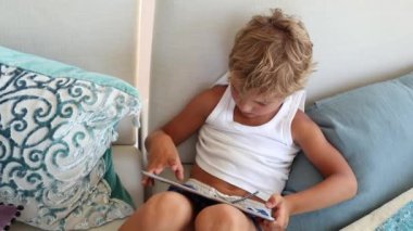 Child playing video-game on tablet. Kid using tech device sitting on couch