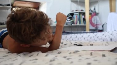Young boy studying at home in front of laptop. Child doing homework lying in bed in front of computer