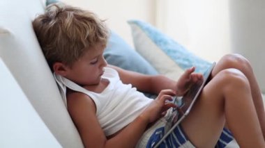 Candid boy playing game on tablet. Child using tech device