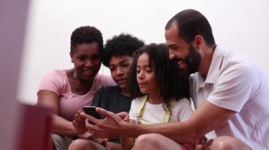 Family looking at smartphone together, mixed race parents and kids holding cellphone at home