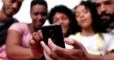 Farklı ırklar arası aileler evdeki koltukta cep telefonuna bakıyor.