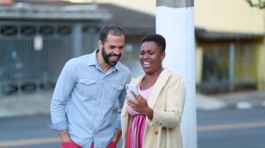 Mix race couple laughing out loud looking at cellphone in street, authentic real life laugh and smile
