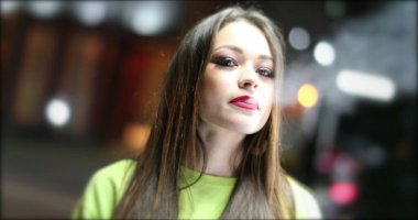 Geceleri sigara içen genç bir kadın. Güzel kız sigara içiyor ve tüttürüyor. Arka planda trafik varken kameraya bakıyor.