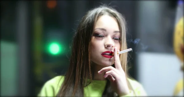 在城市里 年轻女人在晚上抽烟 漂亮的姑娘抽烟 她看着镜头 背景是交通拥挤 — 图库照片
