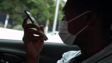 Passenger black man talking on phone in taxi backseat wearing surgical mask