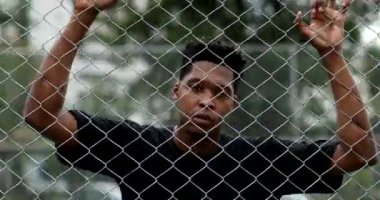 African mixed race man standing behind metal fence. Pensive black guy leaning body thinking