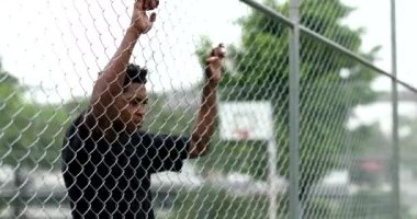 Upset African man leaning on metal fence. Angry black person shaking fence