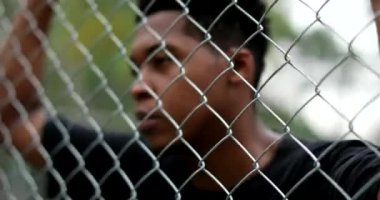 Thoughtful young black man leaning on metal fence at basketball court