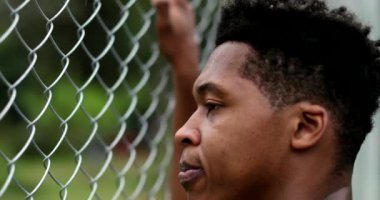 Pensive angry young black man leaning on metal fence outside thinking