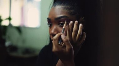 A young woman applying make-up in front of mirror