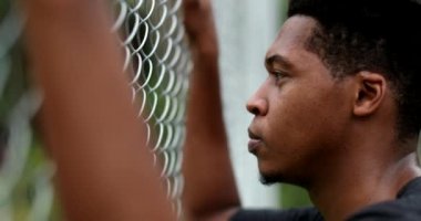 Contemplative young black man leaning on metal fence outside