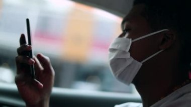 Passenger African man using phone in taxi backseat wearing mask