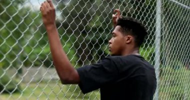 Contemplative mixed race person leaning on metal fence