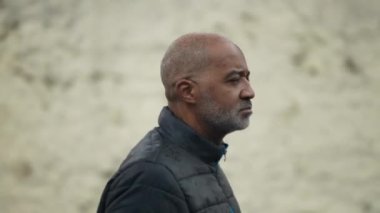A pensive black man walking outside in drizzle a contemplative older person walks in street