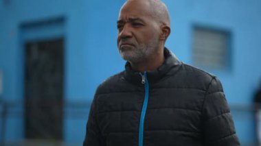 Ciddi bir Afrikalı adam dışarıda çiseleyerek yürüyor.