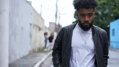 One pensive young black man walking in urban street rubbing eyes and face