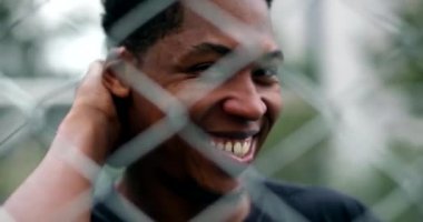 Happy black African man smiling and laughing with metal fence in foreground
