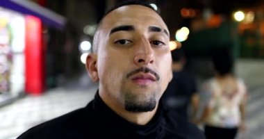 Serious hispanic male looking at camera with serious face standing in street at night