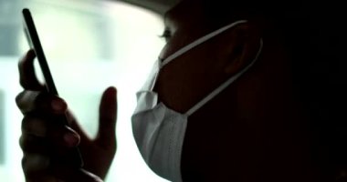 African person talking on cellphone device during pandemic wearing surgical mask in taxi car