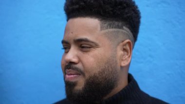 Mavi arka planda, modern saç kesimiyle sokak gözlemcisi dalgın bir genç.