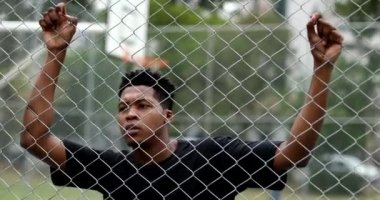 Pensive young black man leaning on metal fence. Contemplative mixed race person