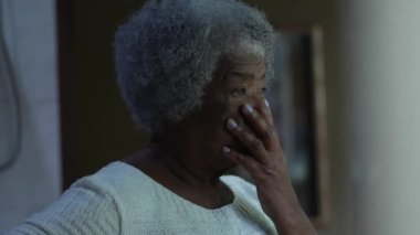 Endişeli yaşlı siyahi bir kadın pencerenin kenarında durmuş endişeli bir Afrikalı yaşlı bayana bakıyor.
