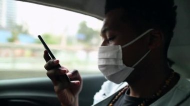 Passenger black man talking on phone in taxi backseat wearing surgical mask