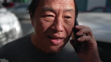 Asian American man speaking on phone in urban street. Portrait of a middle aged person holding smartphone listening