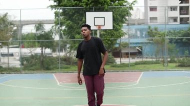 African American young man staring at camera standing outside at basketball court outside