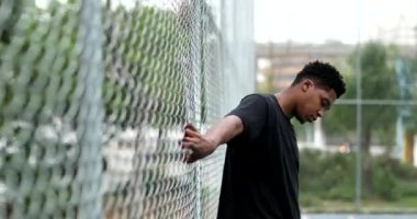 Black guy at basketball court holding into metal fence posing