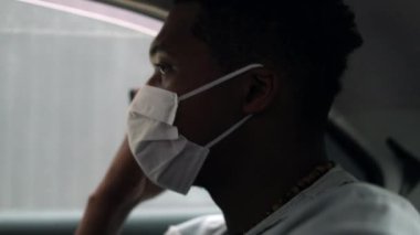 Passenger African man using phone in taxi backseat wearing mask