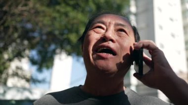 Smiling happy middle aged Asian man speaking on cellphone in street. Happy Person holding smartphone in ear. Portrait guy in conversation