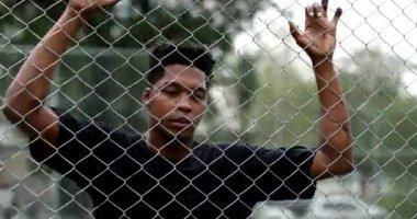 Pensive black guy leaning on security metal fence