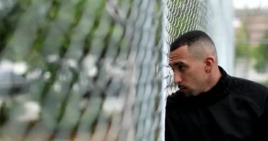 Pensive hispanic man leaning on metal fence looking at camera. Latin guy portrait