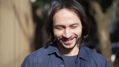 Young man walking in sunlight in city street. A hispanic South American person walks outdoors getting sunshine