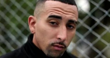 Pensive hispanic man leaning on metal fence looking at camera. Latin guy portrait