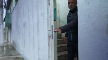 Üst sınıftan bir adam sokağa adımını atar ve ön kapıyı açar.