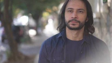 A casual contemplative hispanic young man walking in street with sunlight. Pensive South American guy walks forward in city