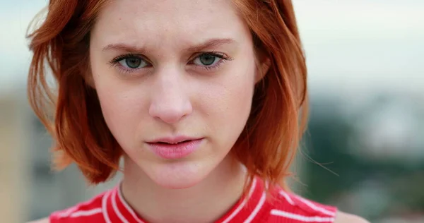 Portrait of young redhead woman adjusting hair with serious and dramatic look