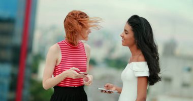 İki bayan arkadaş cep telefonu medya cihazında bir şeye gülüyorlar.