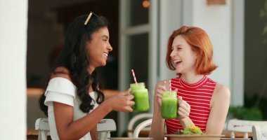 Sağlıklı yeşil meyve suları içerken gülen ve gülümseyen iki güzel etnik kız.