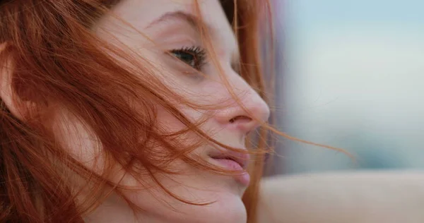 Profile of redhead young woman stretching neck feeling wind outside