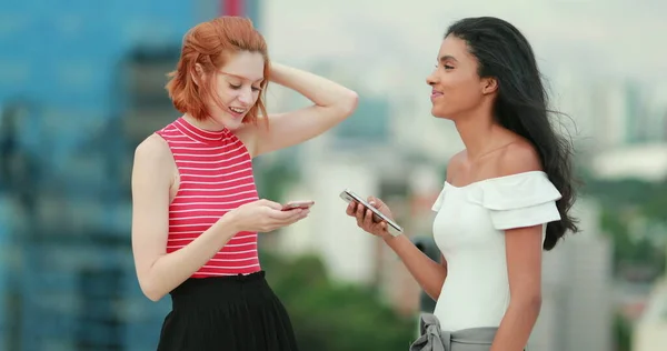 2人の若い多人種の女性が携帯電話の画面上で面白いものを見て笑い出した — ストック写真