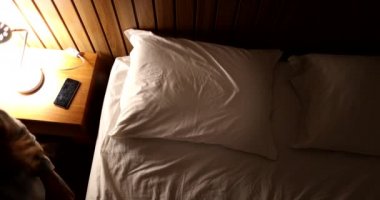 Young woman lies in bed going to sleep, turning night-stand light lamp off