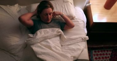 Anxious woman unable to sleep turns on light on, tossing and turning in bed