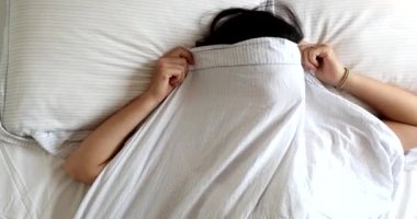 Funny young woman playing hide and seek peekaboo under blanket in bed