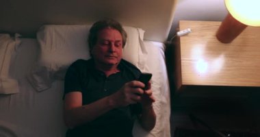 Man checking phone at night in bed, top view. Old Senior person using smartphone