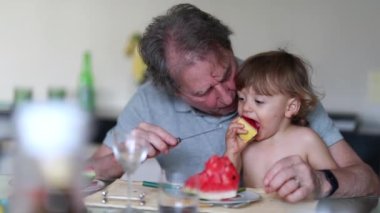 Candid family moment between grand-father and grand-son together eating watermelon fruit